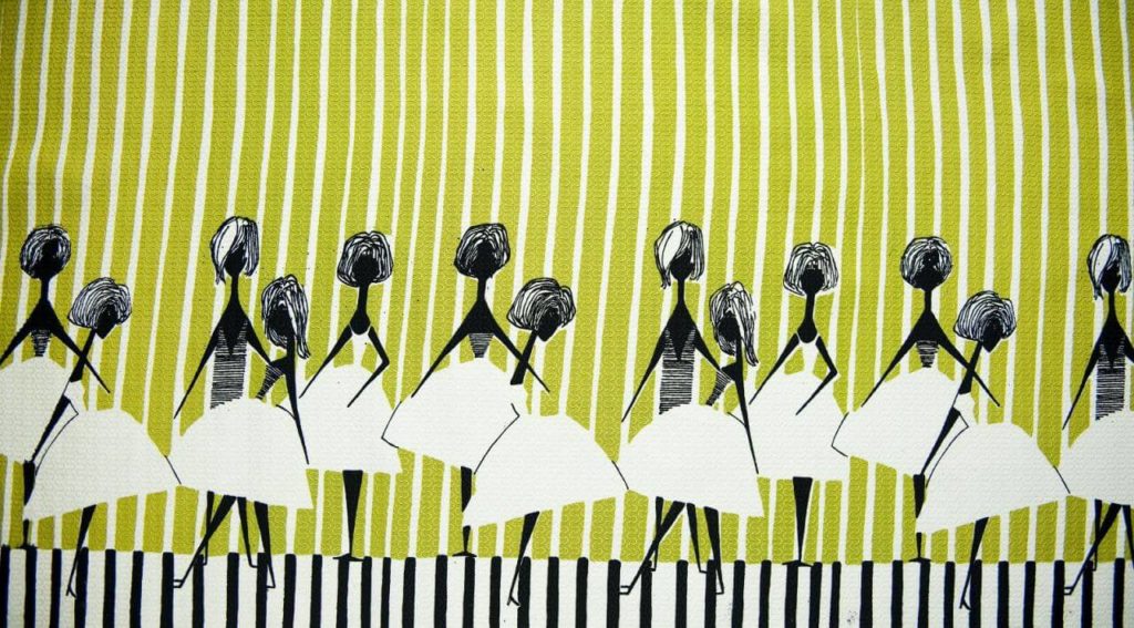 A decorative graphical image of thirteen young women wearing the same type of flared white dress. They all have black, skinny bodies with no facial details. The image is embedded on a green piece of fabric that is intercut with white vertical stripes. For a change, the bottom part of the cloth is white with black stripes.