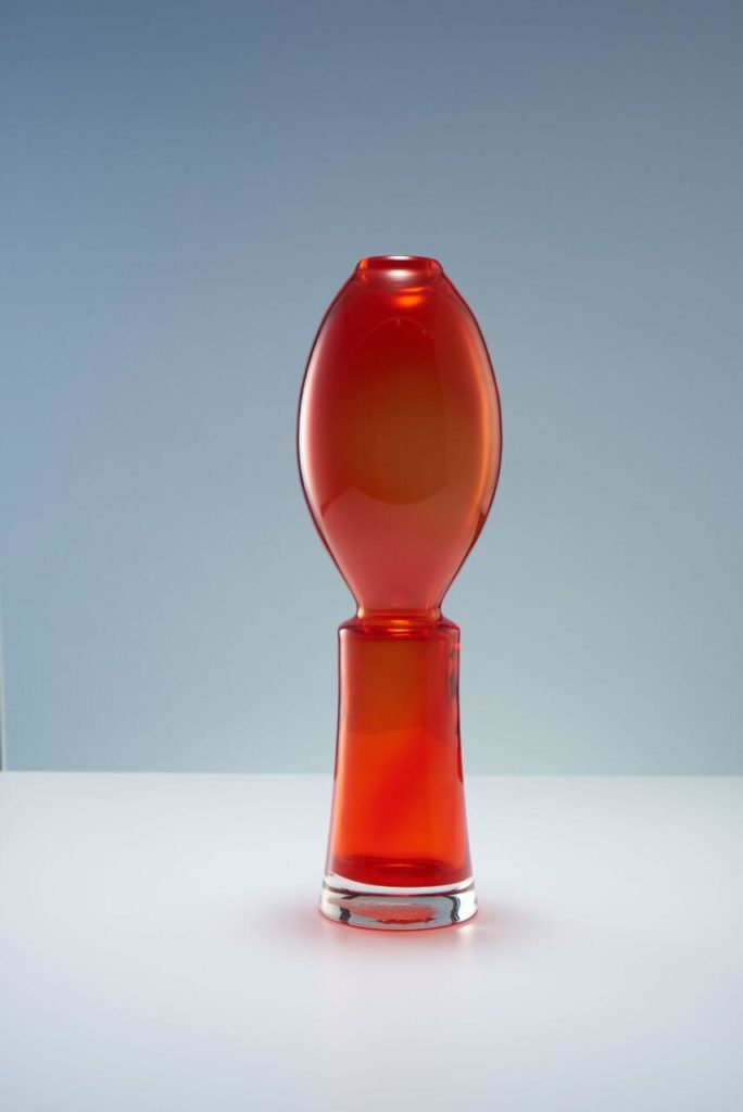 A dark-red vase with that looks like a flame and a candle. Its lower half is conical, while the upper half resembles a massive elliptic bubble.