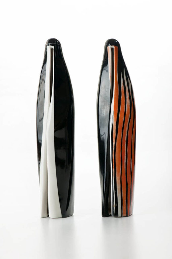 Two thin and tall ceramic figurines depicting Arab women in burkas. The left one is black with white accents, while the one on the right is black with bright-red elements.