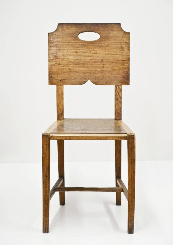 A plain, raw hardwood chair with no additional padding. It has a little round cutout in the backrest.