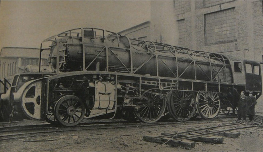 Black and white photograph of a steam locomotive under construction. Part of its body is covered with scaffolding.