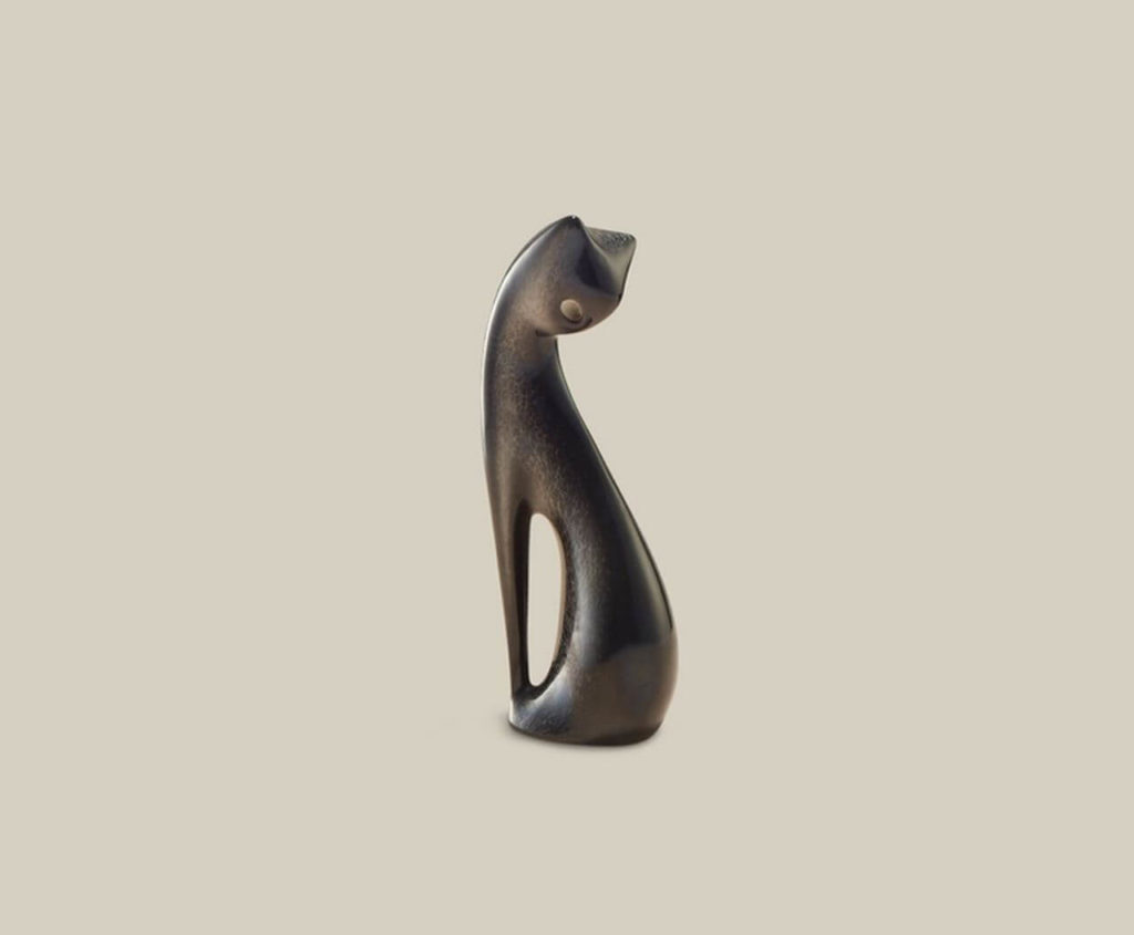 A ceramic figurine of a black cat sitting. Its head is turned back, facing ground.