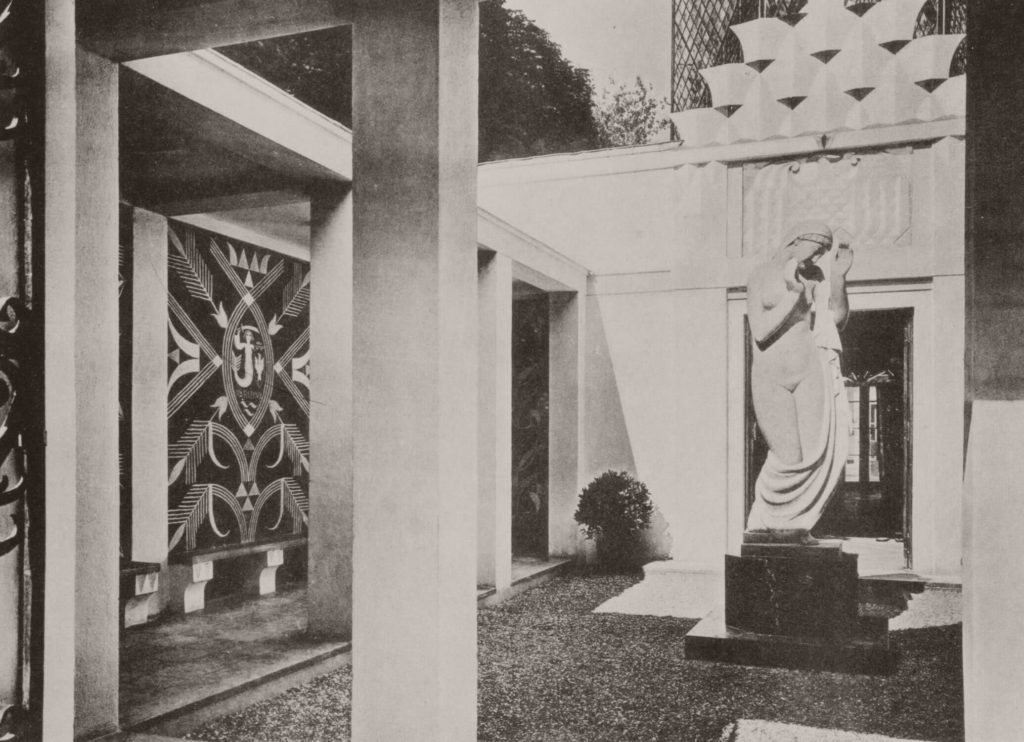 "An old monochromatic shot of the Polish Pavilion's atrium. A sgraffito-decorated wall may be found on the left. A classical-style statue of a grieving naked woman stands on a pedestal to the right."