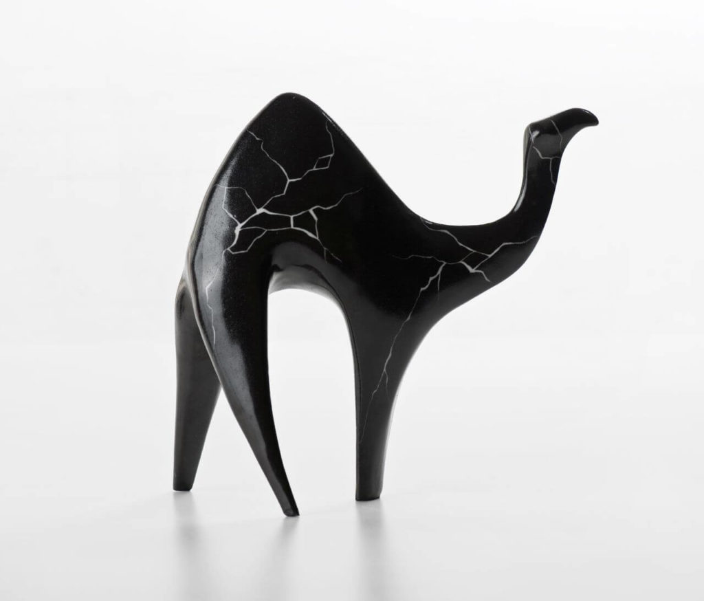 A black ceramic figurine of a camel. Its structure looks as if it were a little cracked.