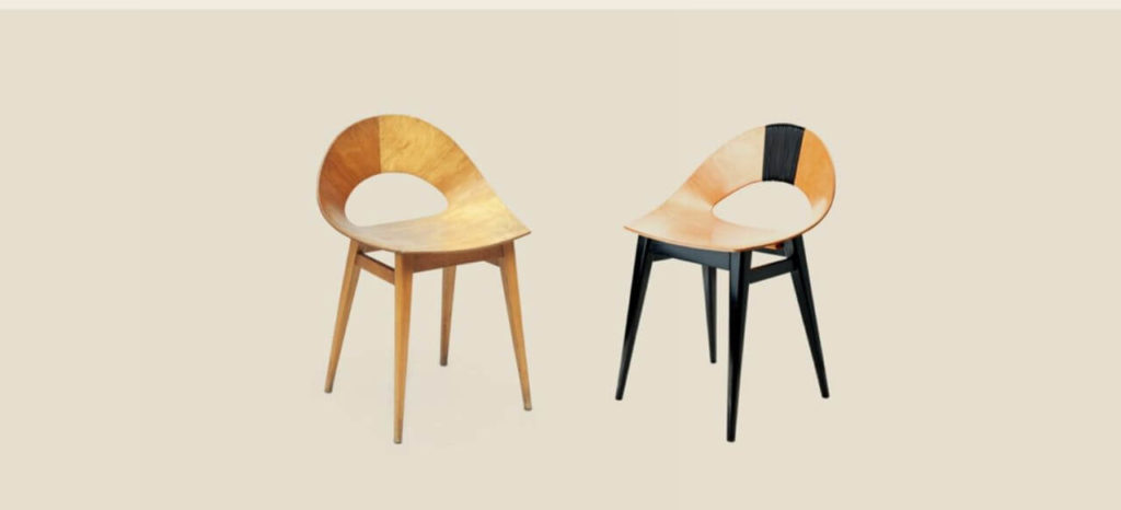 Two wooden chairs with round and low backrests, resembling the shape of a shell, The left one is brighter and has light-brown legs. The right one has black legs and a wide black stripe on the back.