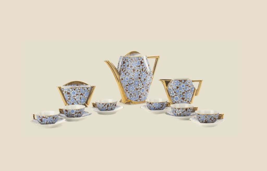 A full tea set. Six cups on saucers, a teapot, a milk jug and a sugar bowl. All are decorated with blue flower ornaments. Their handles are golden. The inner sides of the cups and the bottoms of the saucers are white.