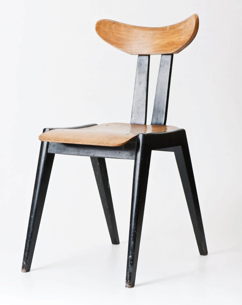 A chair made of wood. It has black legs and a backrest with two black vertical lines and a bright, slightly curved horizontal section on top.