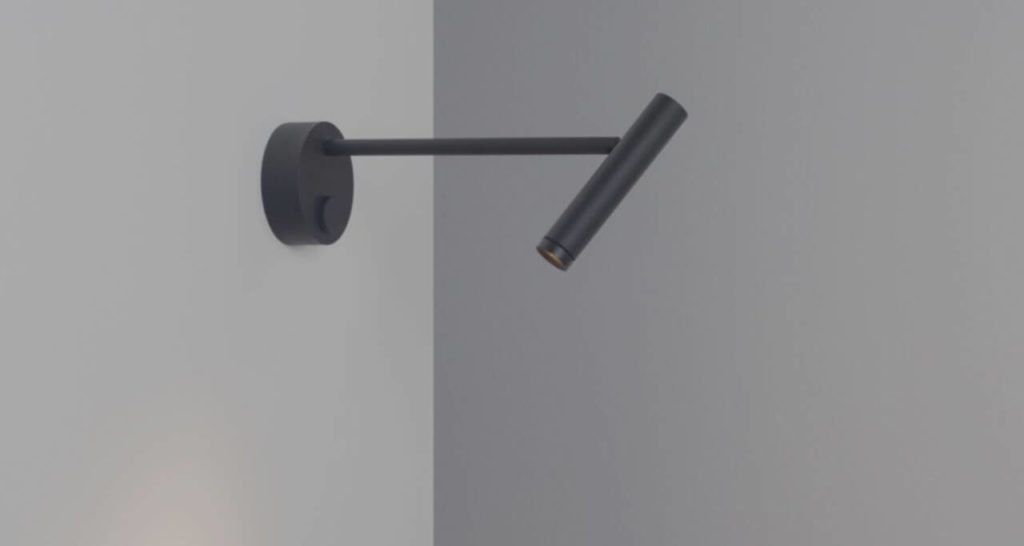 A black wall lamp consisting of a round base fixed to the wall with an on/off switch, from which a spotlight protrudes. The object is shaped like a desk microphone but suspended horizontally.