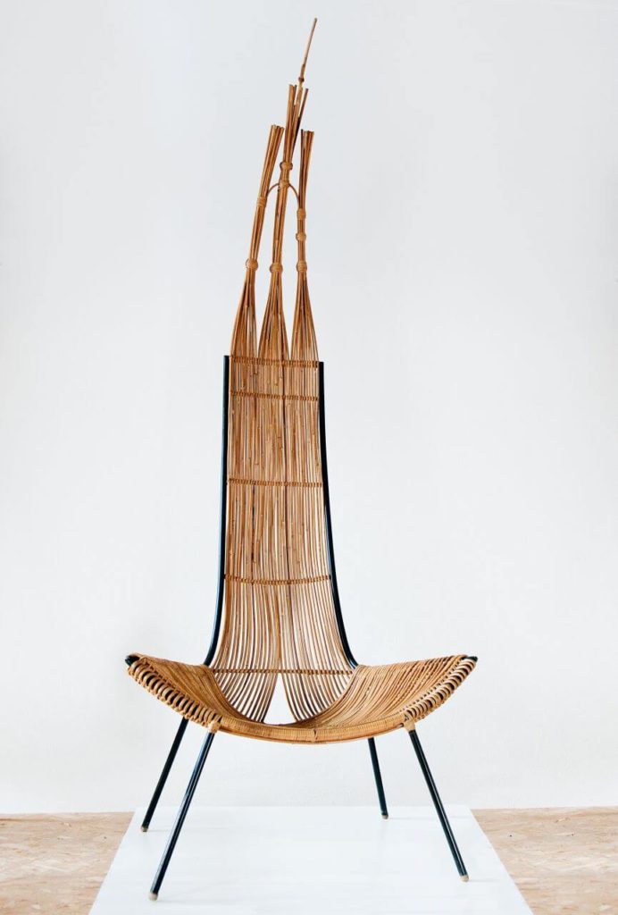A wicker chair. Its seat is placed surprisingly low, while its back is disproportionately tall and resembles a gothic tower.