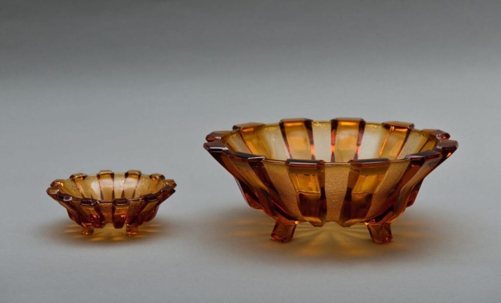 A gablet and a cup are two decorative round translucent glass dishes. They have a warm, dark brown colour. Underneath the objects, a faint light reflection may be detected.