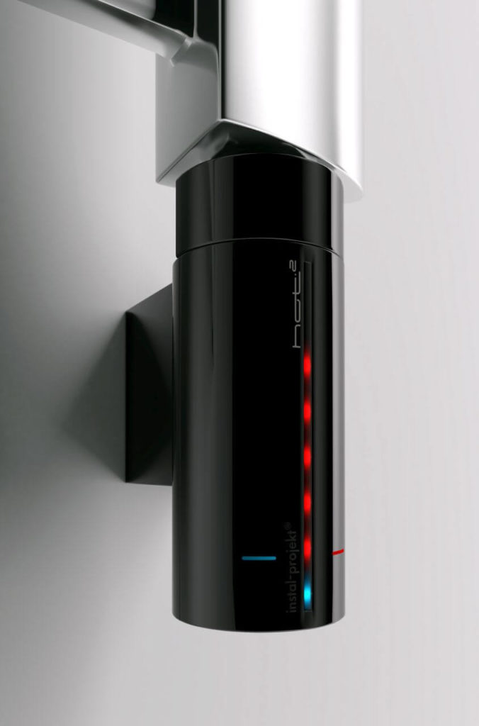 A cylindrical, black, glossy, vertical object attached sideways to the wall and fixed to the radiator from above. It has a measurement with lights glowing red or blue. A white manufacturer's logo is visible.