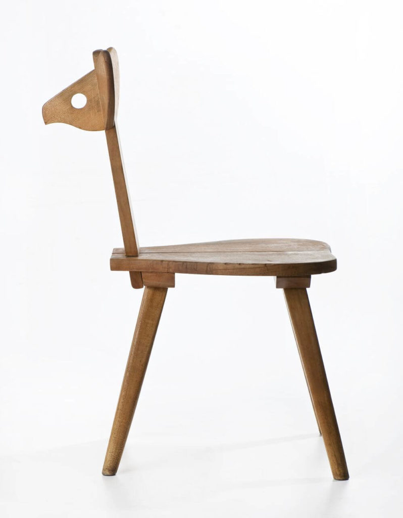 A wooden chair in the shape of a young deer. The back of the chair resembles the animal's face, while the seat resembles its body. The legs are long and slim, with a wide spread.