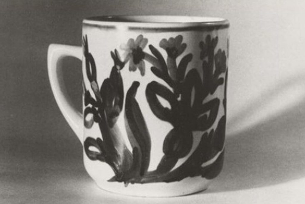 A monochrome photograph of a white teacup with a simple flower artwork.