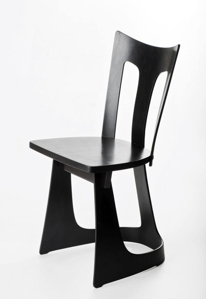 The edges of a black chair are slightly curved. It features two cutouts on the back. There are no armrests, and one base connects the three legs.
