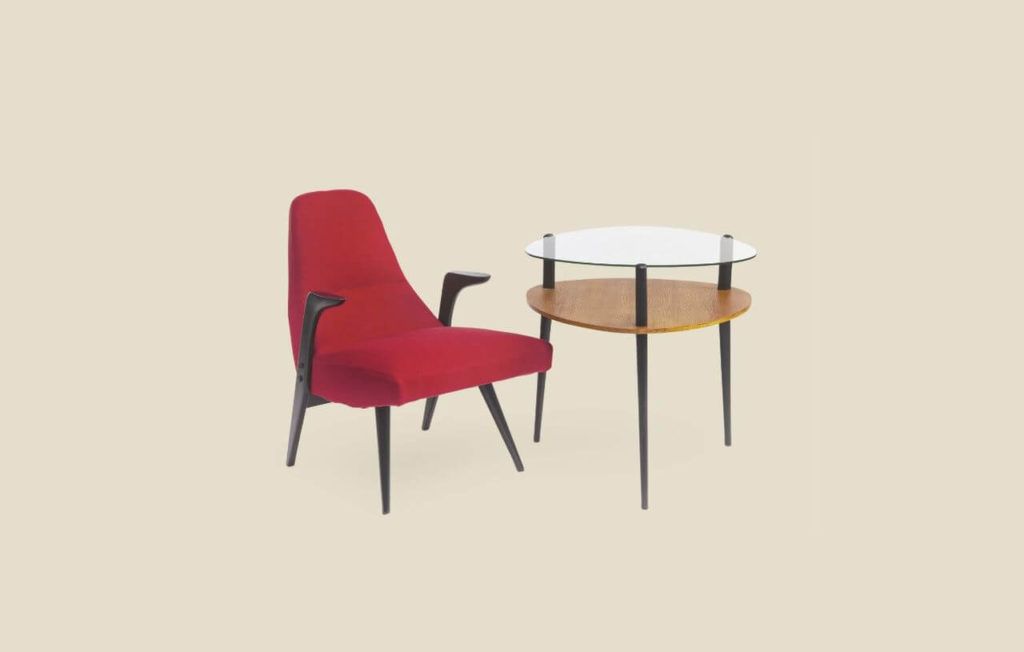 An armchair and a table are depicted in this image. On the left, there is an armchair. It is red and constructed out of a supple cloth. It has tiny, black legs. The black armrests, which are also extensions of the two back legs, are rather short. The table has a transparent glass tabletop with a round wooden shelf beneath it. It stands on three black, stick-like legs.