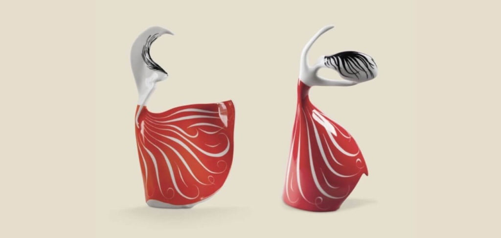 Two porcelain figurines depicting dancing women in long red dresses with white wave-like pattern. Their bodies are white, and their hair is black. No facial features are visible.