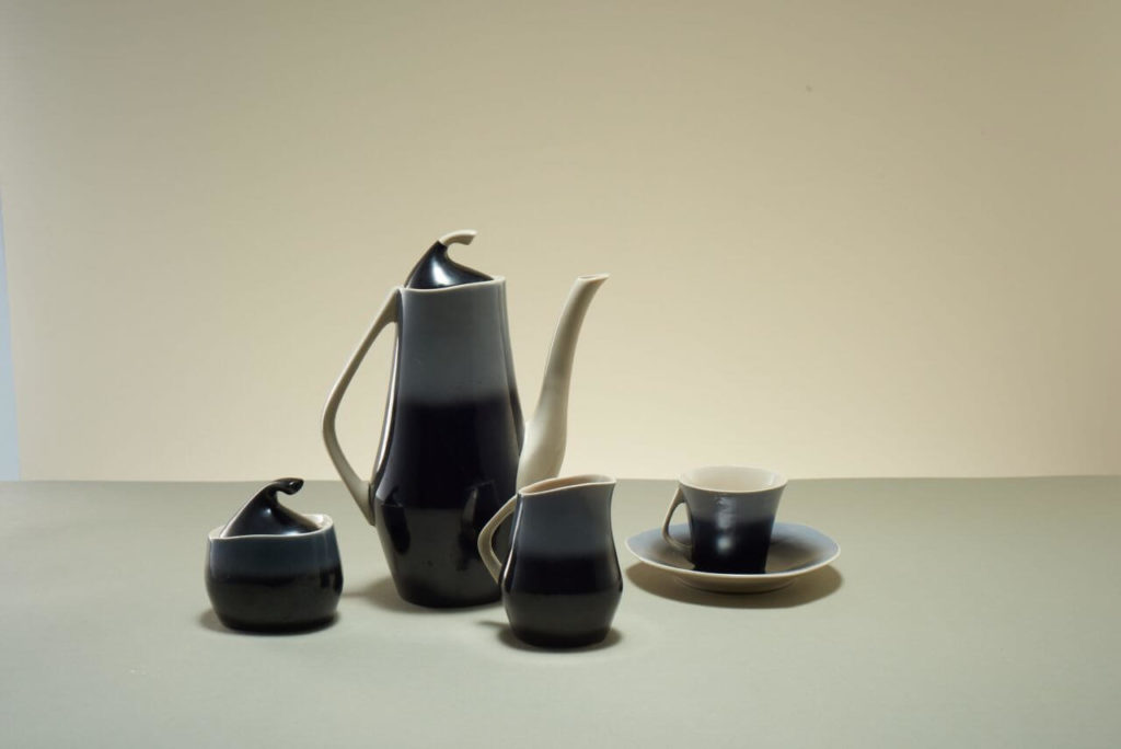A coffee set consisting of a coffee pot, a milk jug, a sugar bowl, and a coffee cup. All items are black with some white accents. Their inner sides are mostly white, with some brown undertones. They are tall and have soaring shapes.