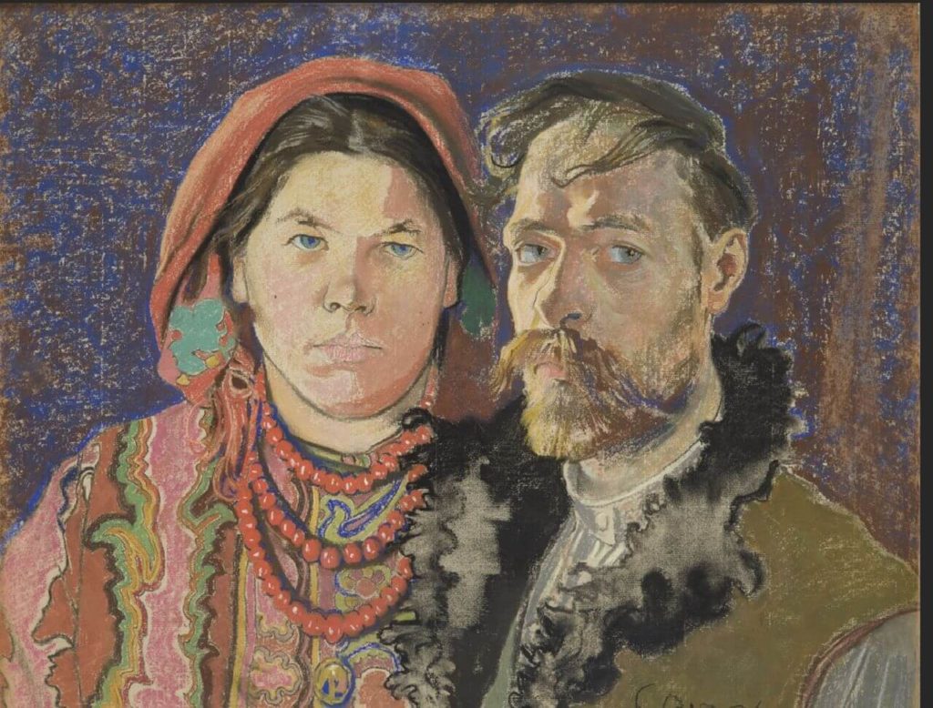 A pastel drawing. It is a portrait of a middle-aged couple. The woman on the left has long black hair hidden under a red scarf. She is wearing a necklace of red beads and a colourful blouse. The man on the right has brown hair and a brown beard with a long thick moustache. He is wearing a brown fur vest and a grey shirt underneath. The woman is looking at a viewer, while the man is looking a little to his left side.