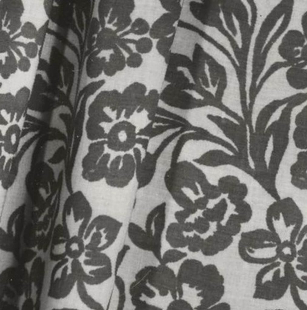 A black and white photograph depicting a detail of a piece of fabric decorated with a flower pattern.