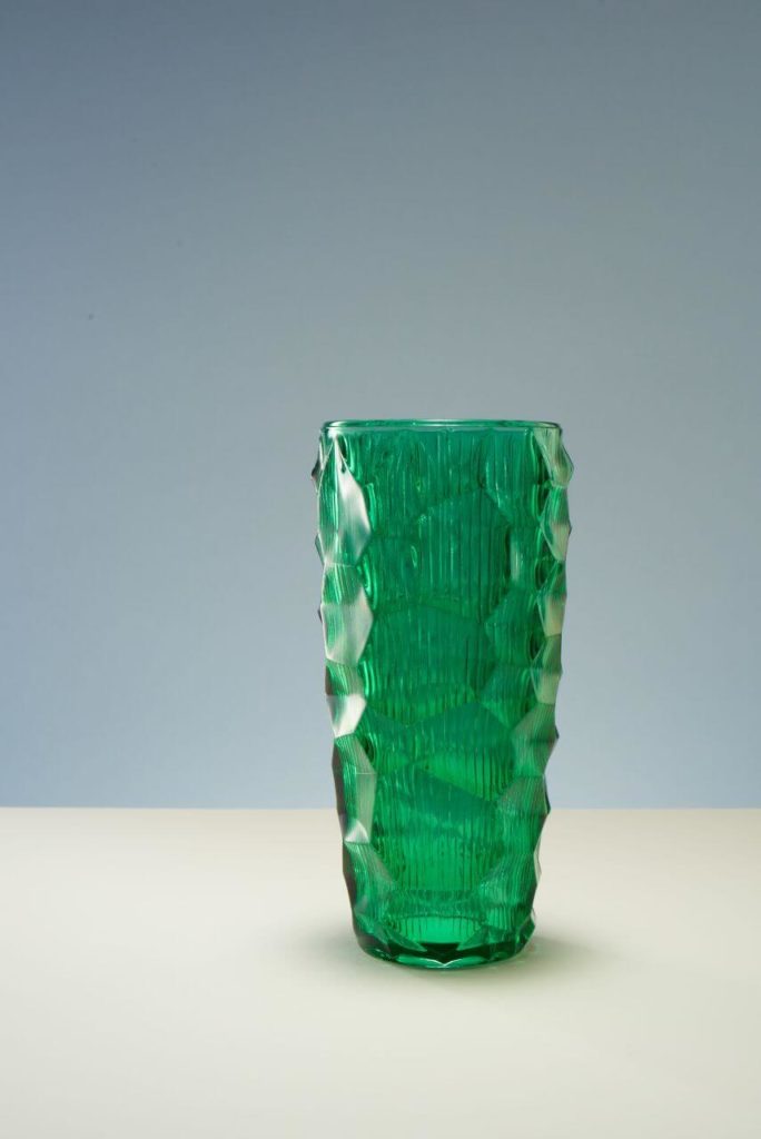 A green glass vase. 'It resembles a sculpture, carved as if with a chisel on the outside, with a pattern of light-reflecting graphical incisions running outwards from within'. Its shape is raw and highly irregular.