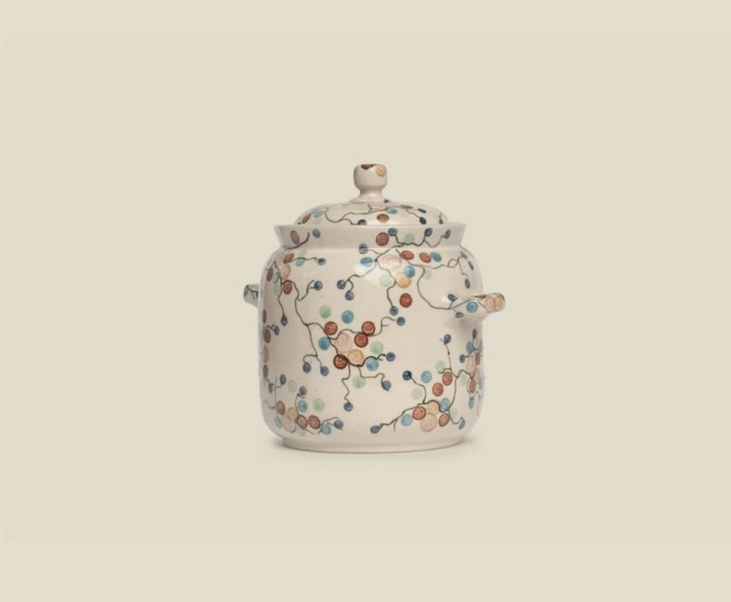 A ceramic jug with a lid and two handles. It is white, decorated with painted stems and purple and brown berries.